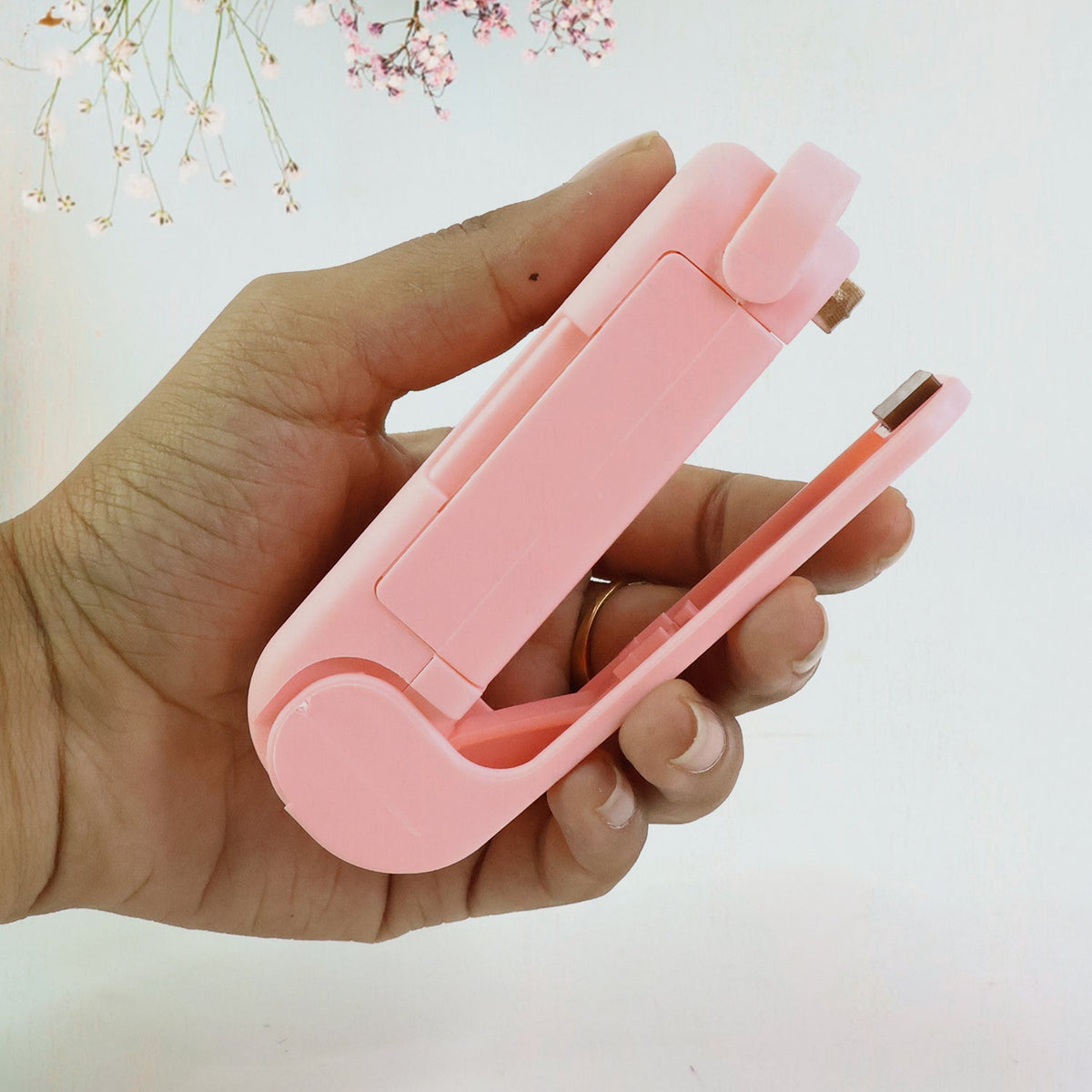 A hand holds the pink plastic bag sealer, showing its compact size and open sealing mechanism.