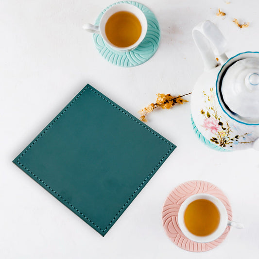 Set of four square brown Leather Tea Coasters arranged neatly on a wooden dining table.