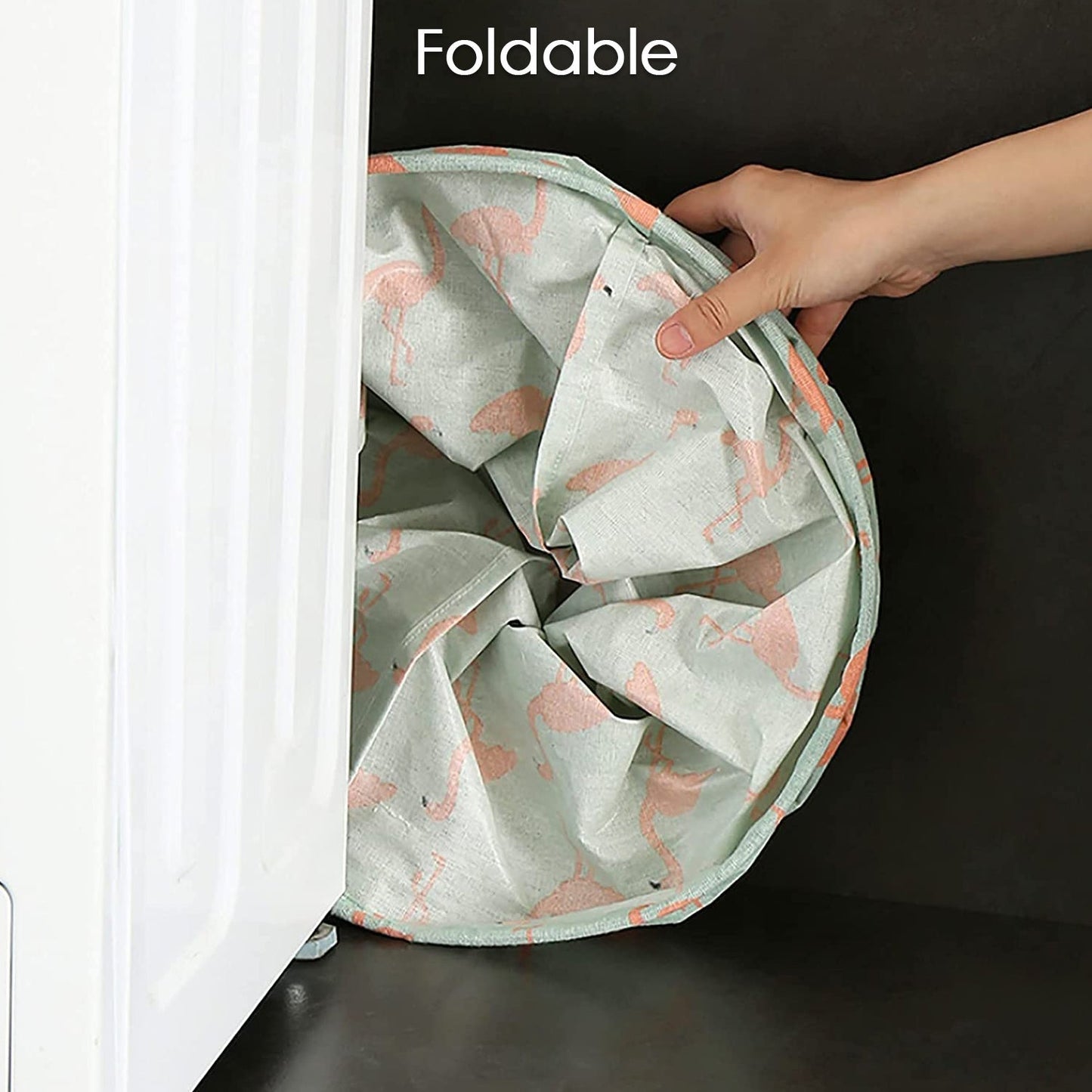 A hand compressing a flamingo-patterned fabric laundry hamper to demonstrate its foldable design, fitting into a narrow