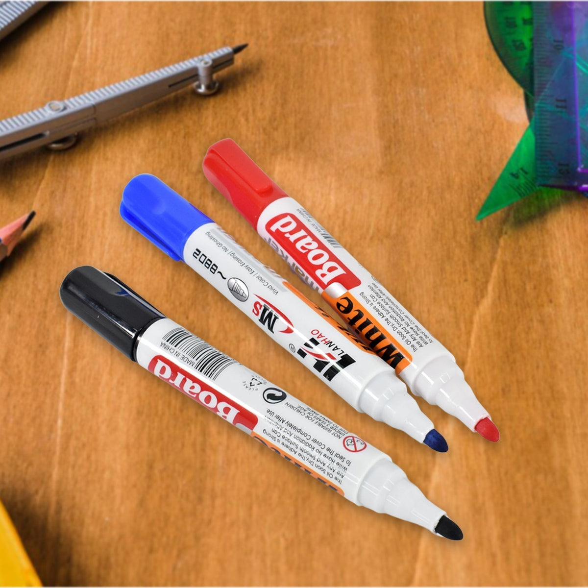 Three whiteboard markers in black, blue, and red, with their caps on, lying on a wooden surface with drafting tools in the