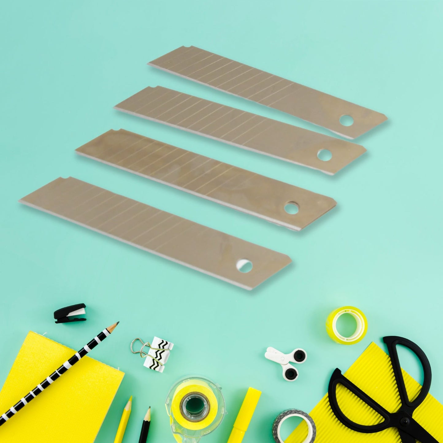 Four silver utility knife blades are arranged diagonally on a light blue background with various office supplies.