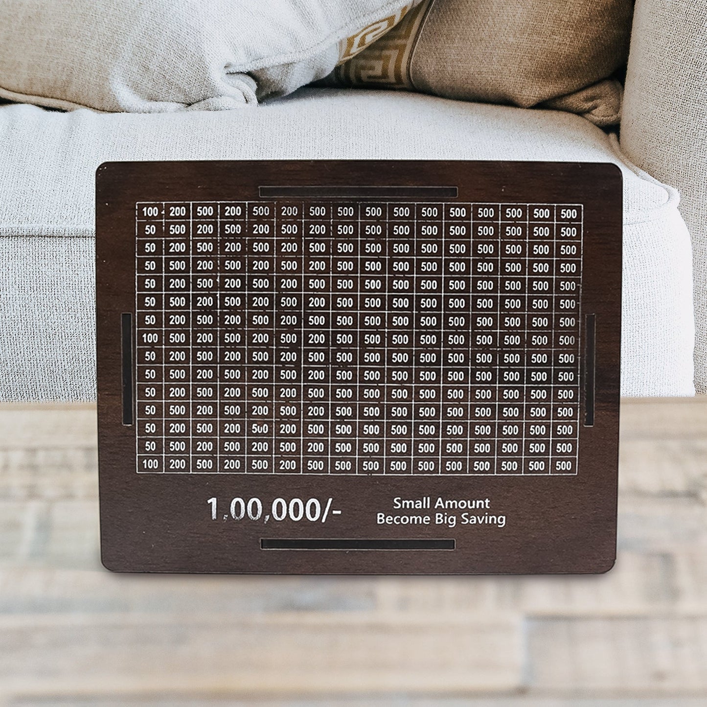 A dark brown wooden savings box with a white grid tracker on a wooden table, with a light-colored sofa in the soft-focus