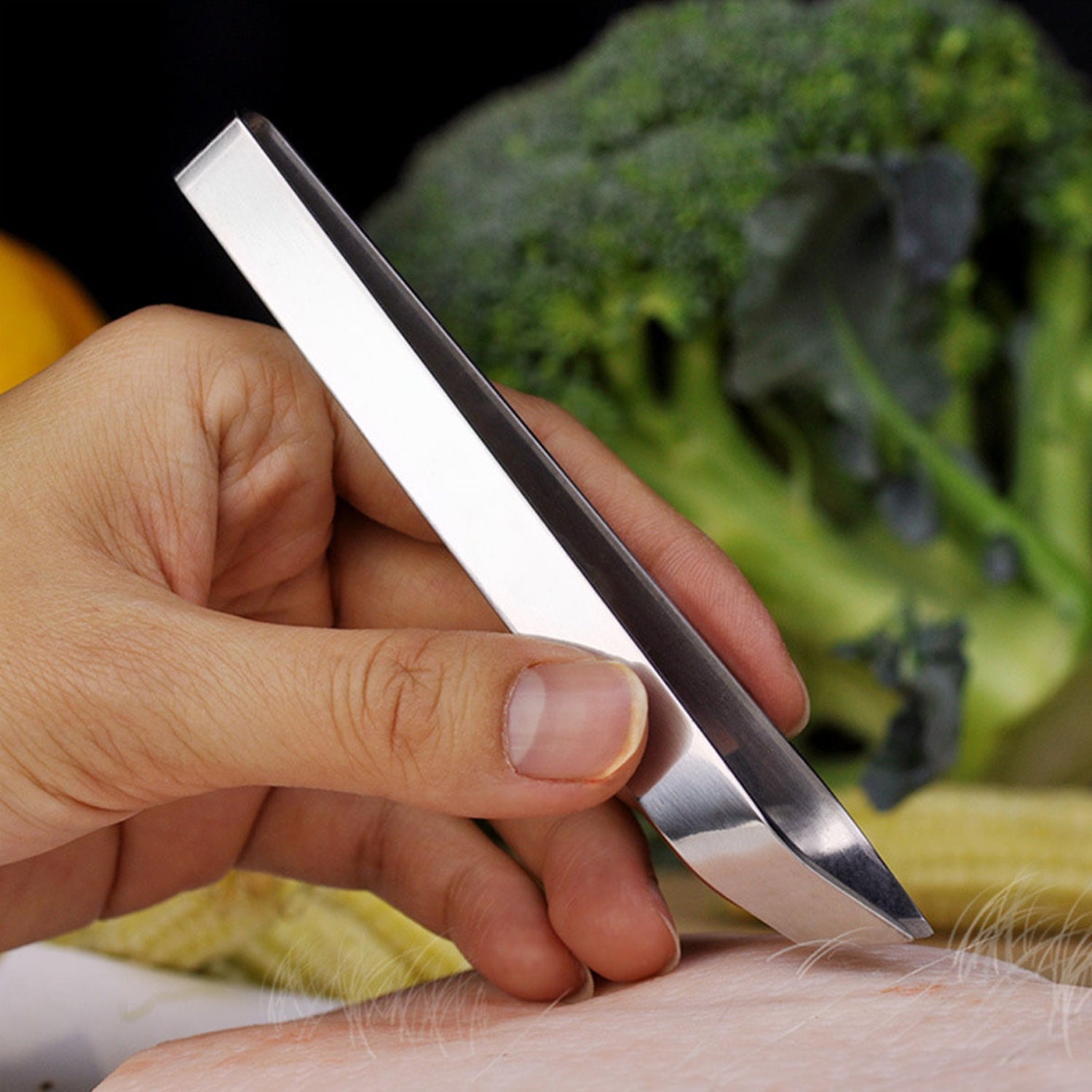 A hand holds silver stainless steel tweezers, poised to pluck hair from a piece of raw meat.