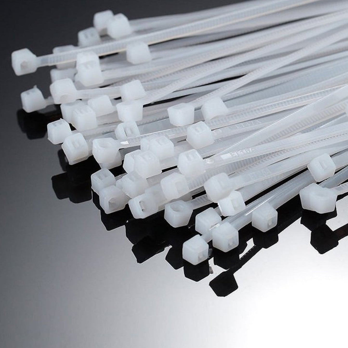 A close-up view of the interlocking heads of many white nylon cable ties on a reflective dark surface.