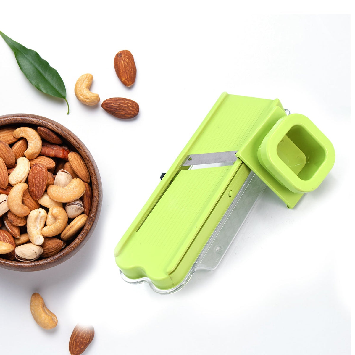 A green plastic slicer with a clear base is surrounded by scattered nuts and a wooden bowl of nuts.