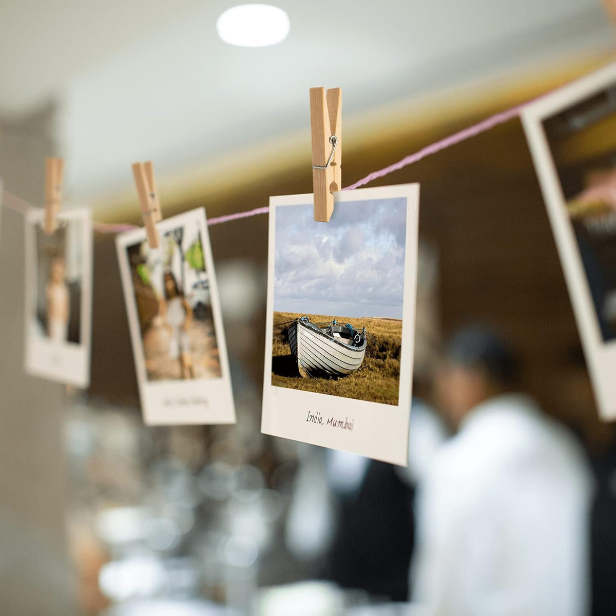 Several bamboo clothes pegs holding small photographs on a pink string, with a blurred indoor background.