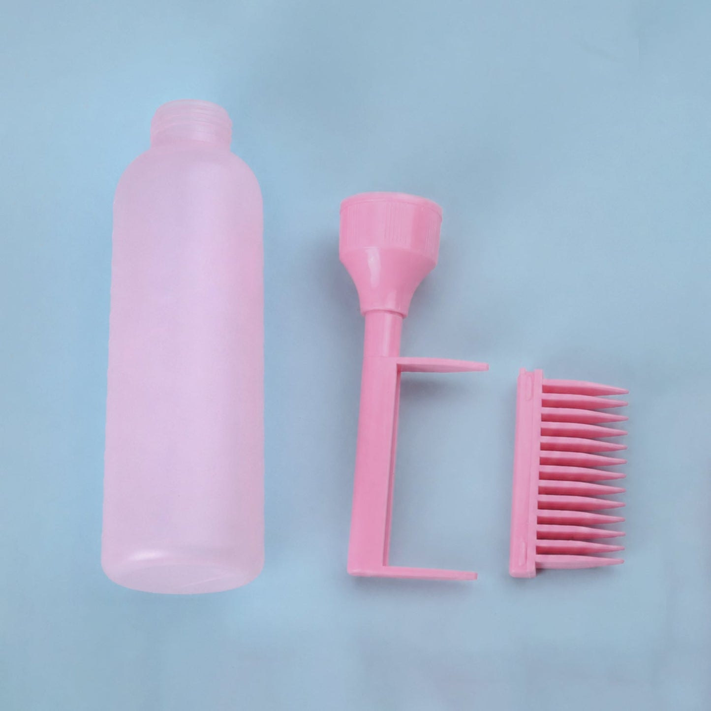 The pink 2 In 1 Hair Oil Applicator Bottle with Scalp Comb is disassembled into three parts on a light blue surface.