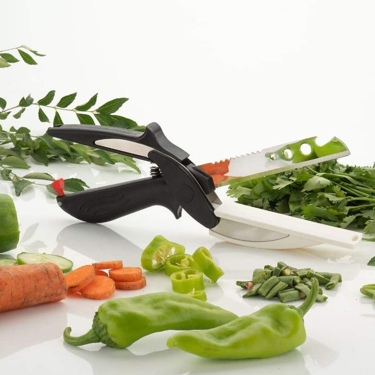 A black and white clever cutter is positioned on a white surface, surrounded by chopped and whole vegetables.