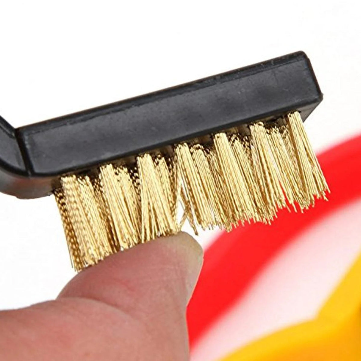 A close-up of a hand touching the brass bristles of a black-handled brush.