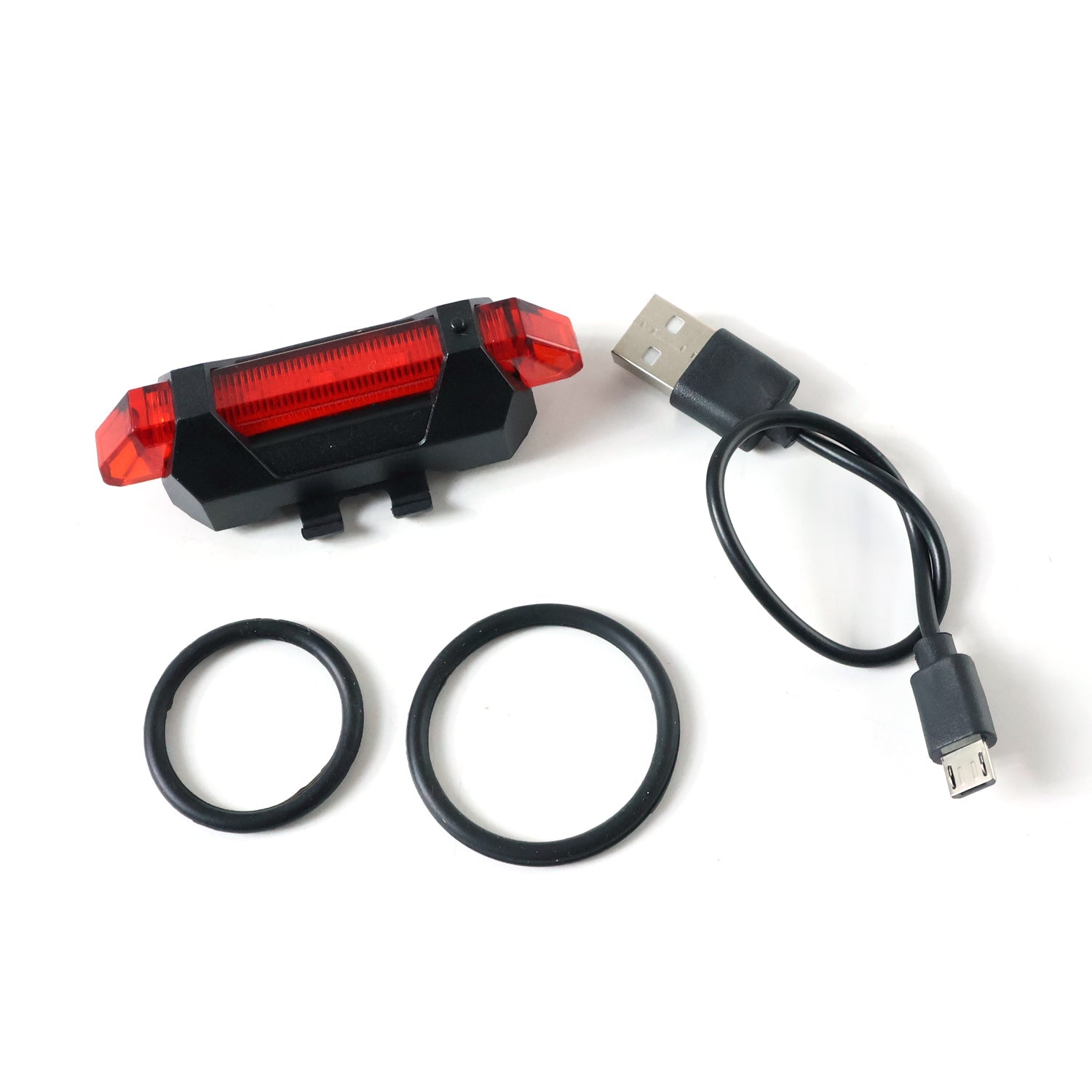 A red LED bicycle tail light, a black USB charging cable, and two black rubber rings are neatly arranged on a white