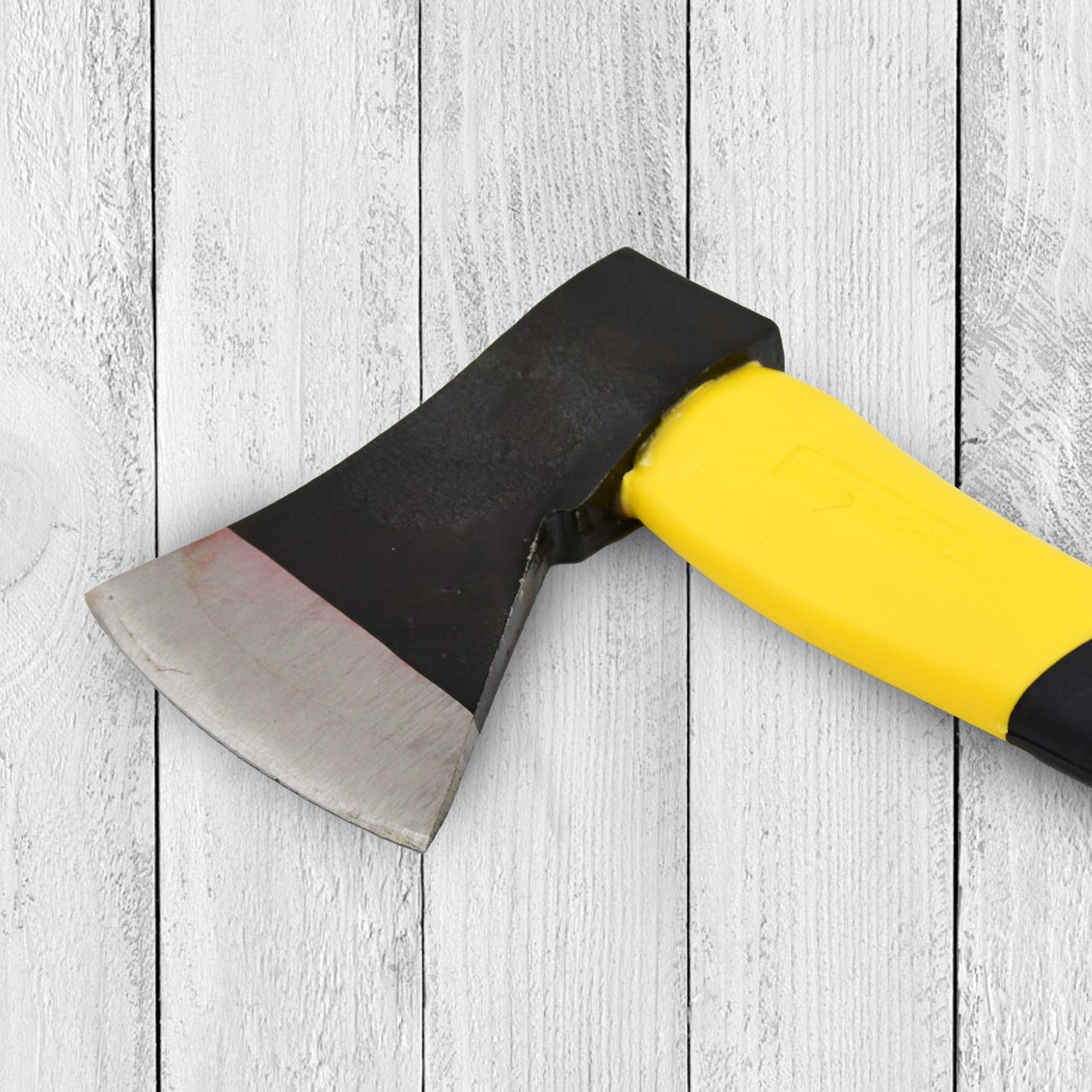 Close-up of the hatchet axe head and part of the yellow and black handle against a white wooden background.