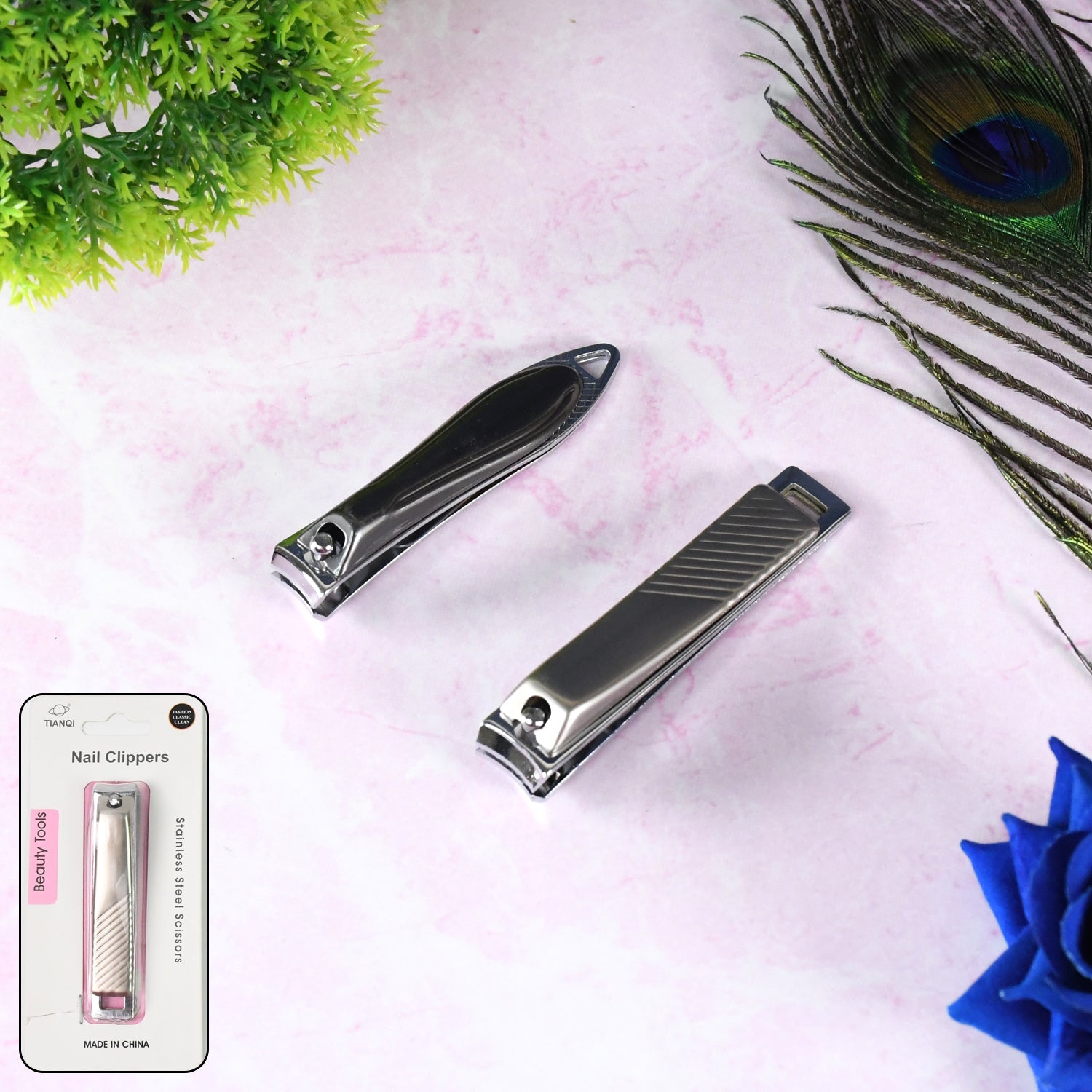 Two stainless steel nail clippers with packaging on a pink surface with a peacock feather.