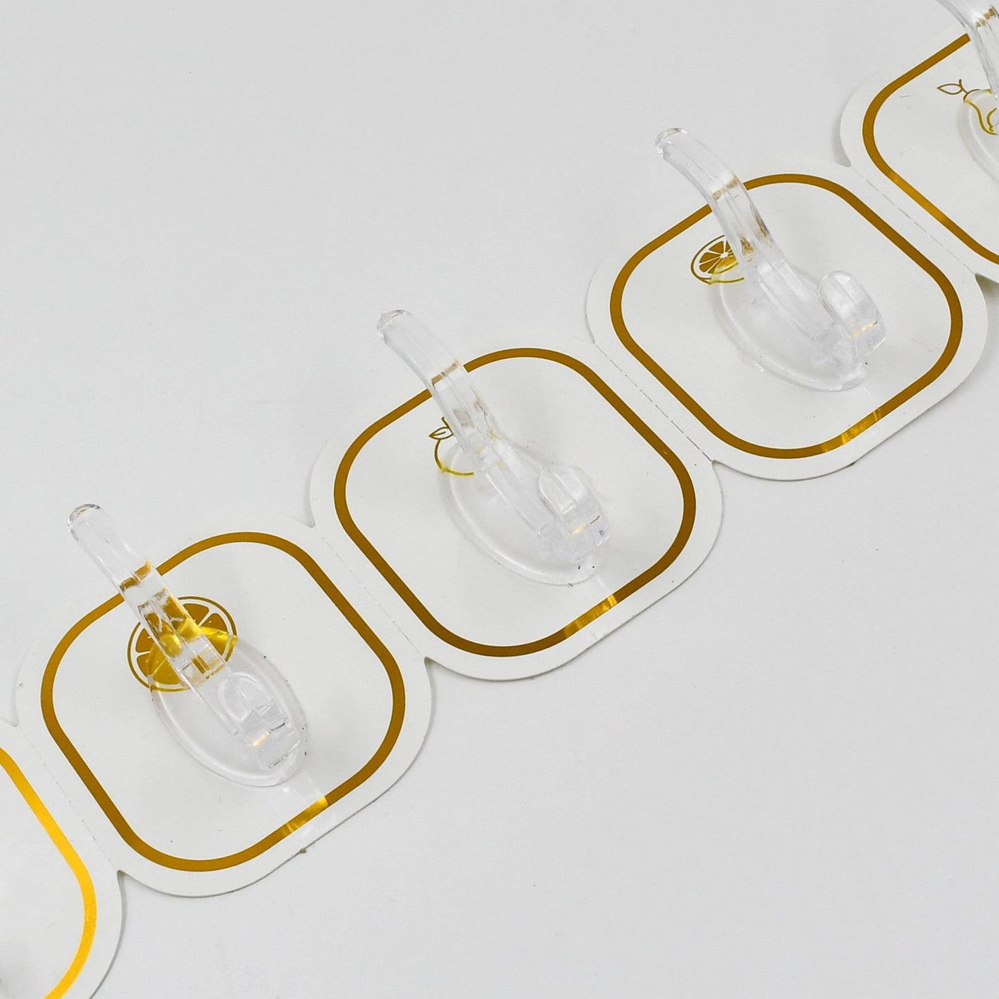 Close-up view of three transparent adhesive hooks with gold borders, showing the clear plastic hooks.