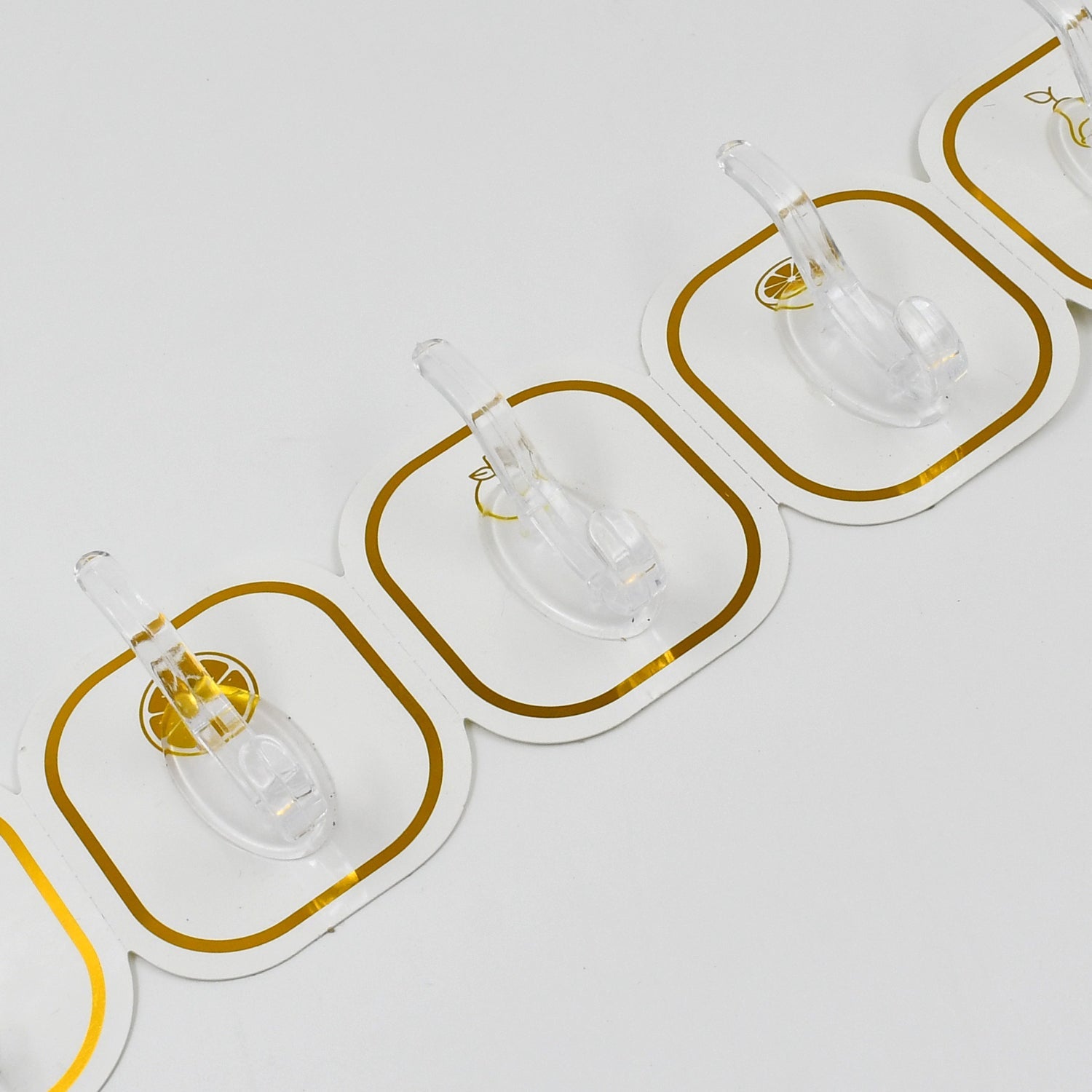 Close-up view of three transparent adhesive hooks with gold borders, showing the clear plastic hooks.