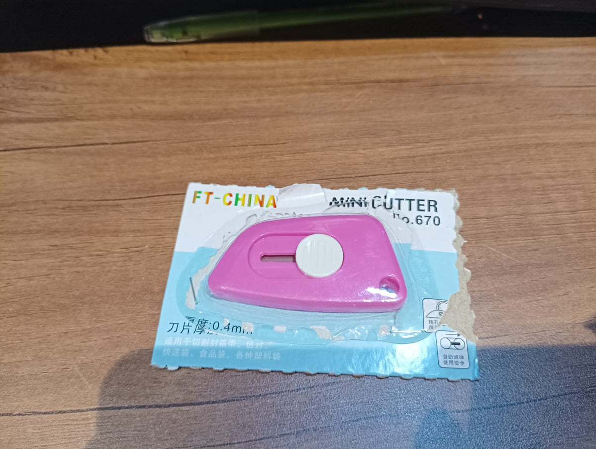 A pink mini cutter in its clear and blue retail packaging, resting on a wooden surface.