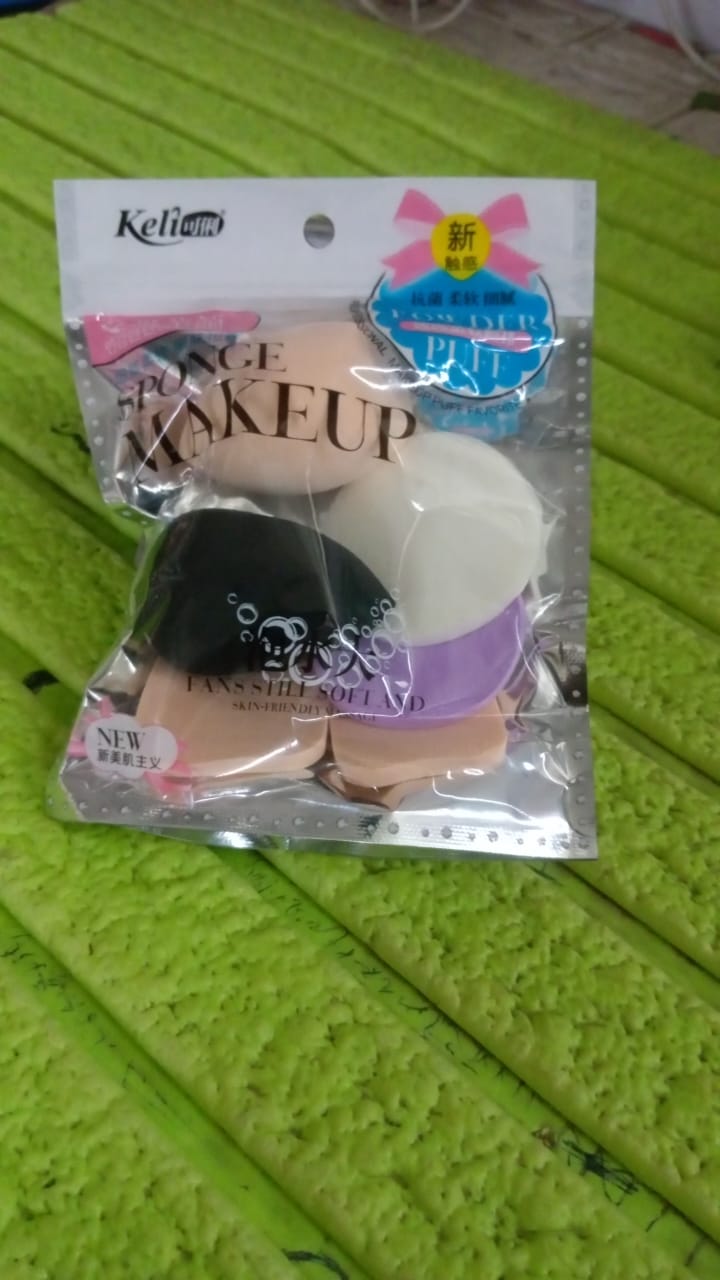 A clear plastic package of Keli brand makeup sponges in various colors and shapes rests on a green textured surface.