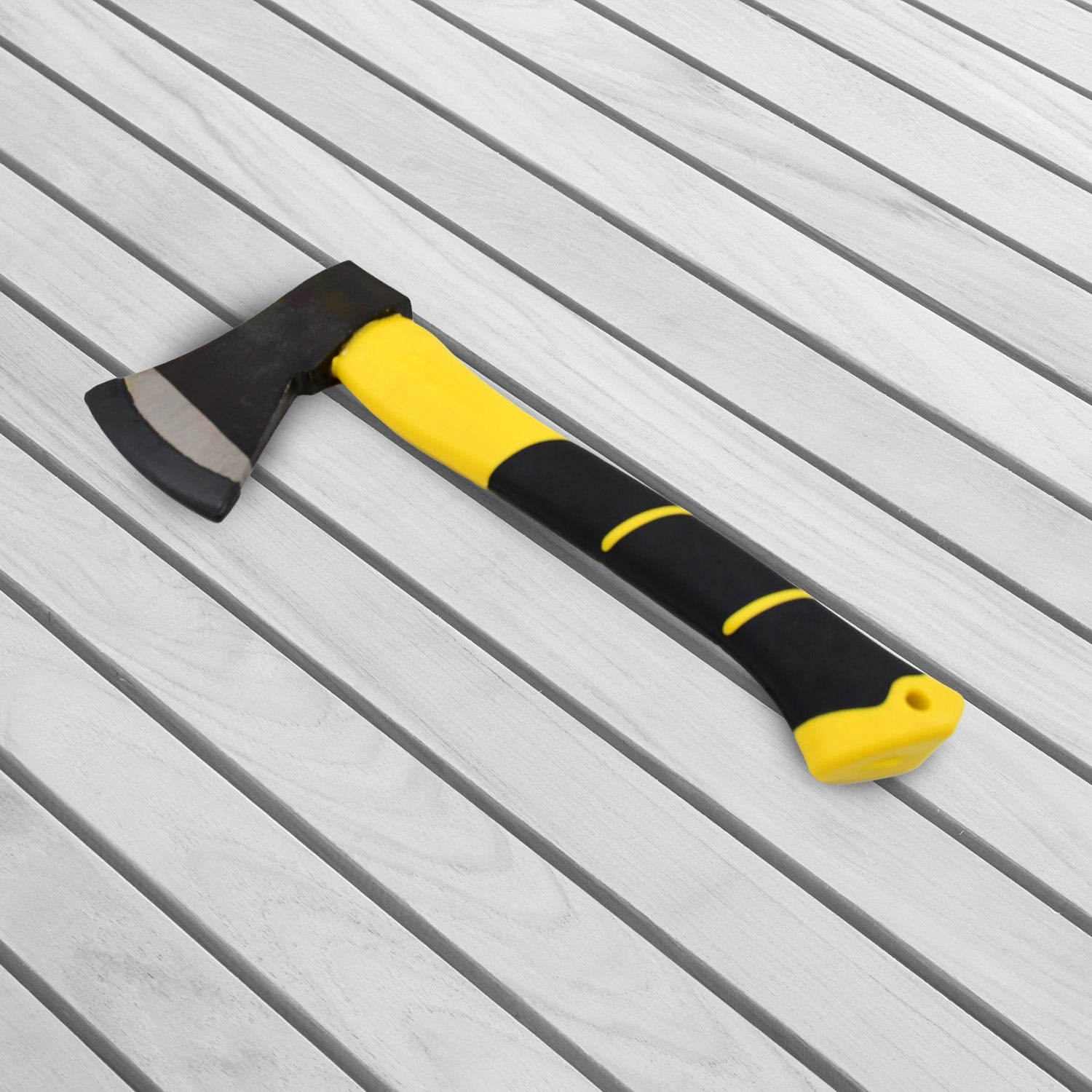 The yellow and black hatchet axe is lying diagonally on a light gray wooden slatted surface.