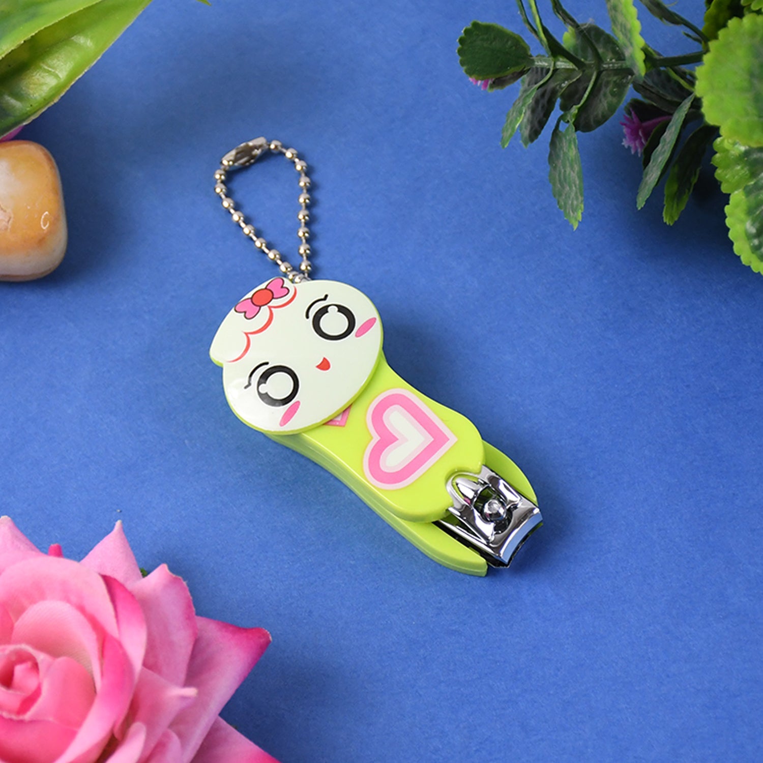 A green and white cartoon character nail clipper with a pink heart and a silver ball chain, on a blue background with a pink