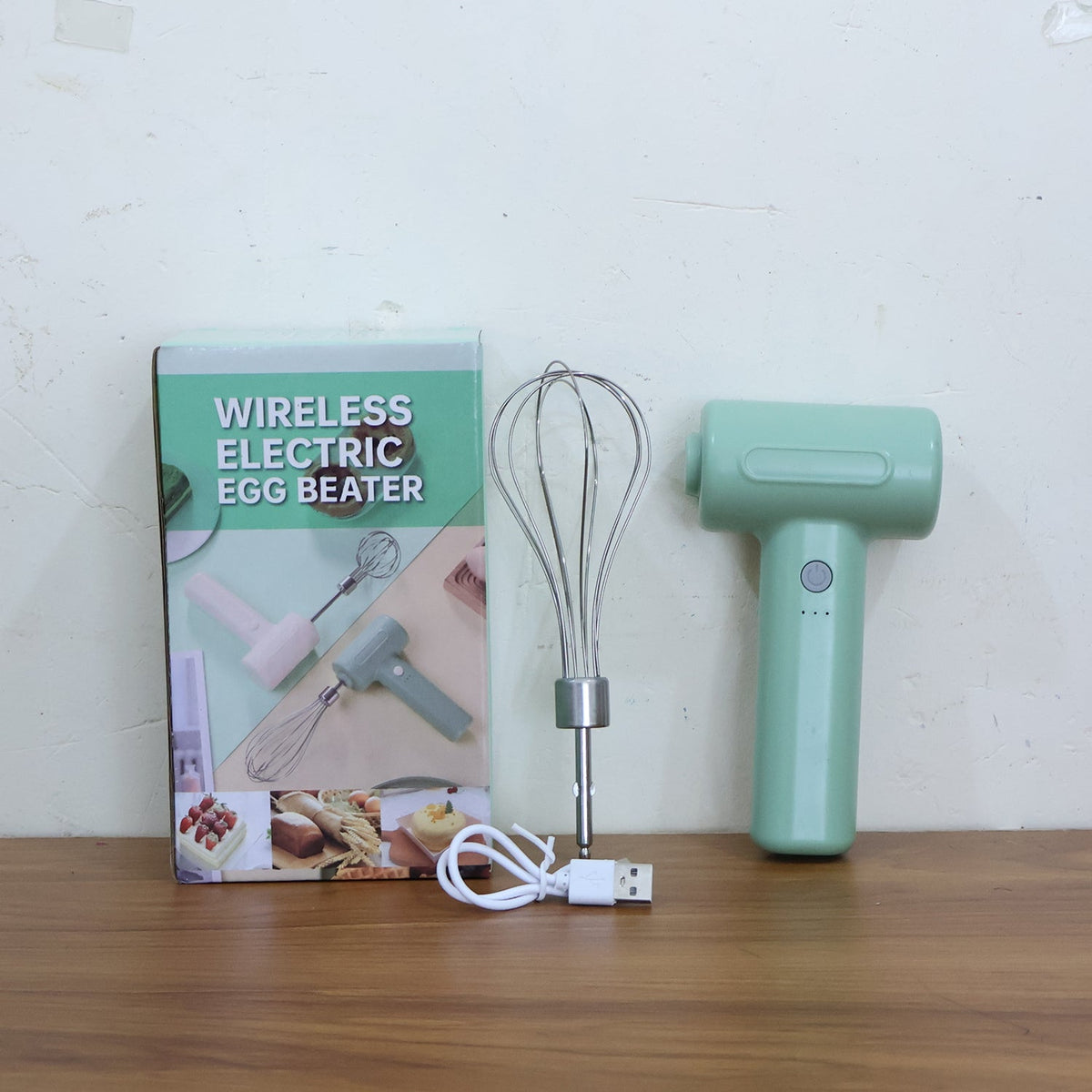 Light green cordless electric whisk, whisk attachment, USB charging cable, and product box on a wooden surface.