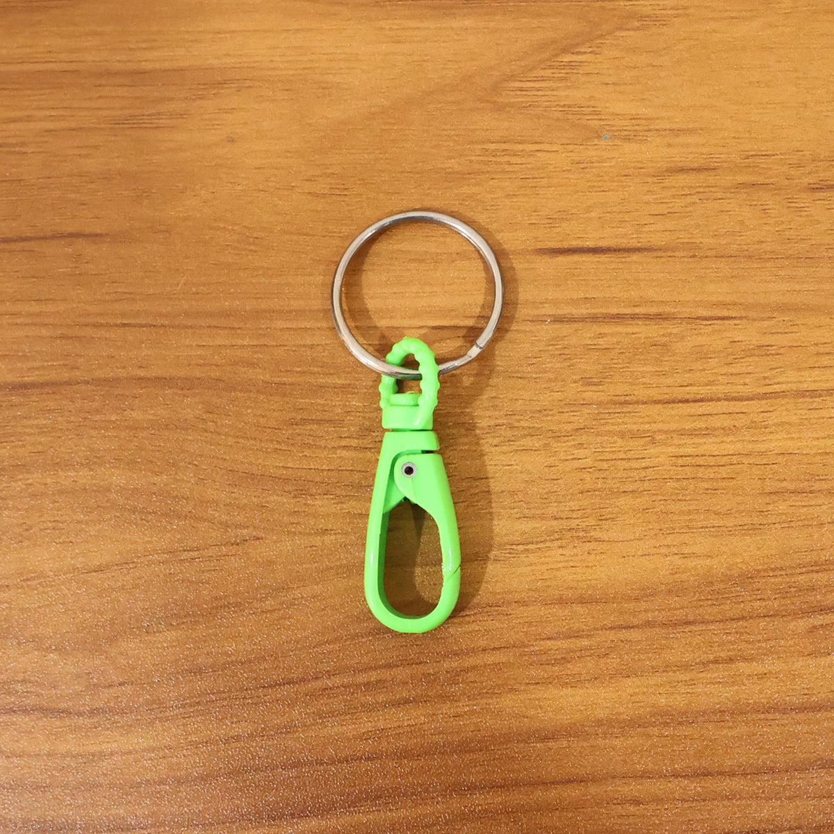 A single green plastic carabiner keychain with a silver ring centered on a light brown wooden surface.