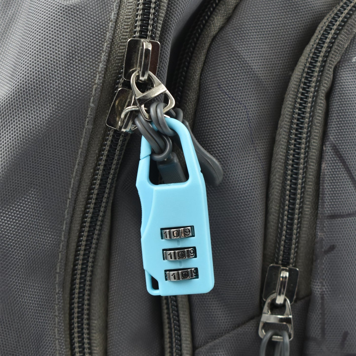A light blue 3-digit combination lock attached to the zipper of a grey backpack.