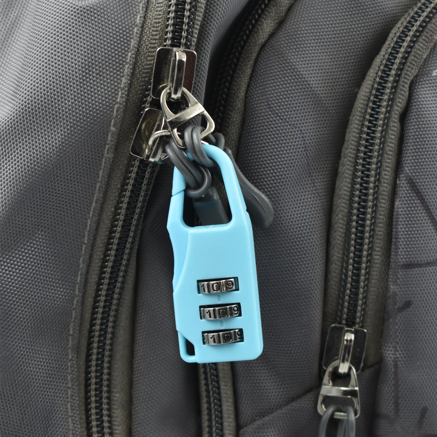 A light blue 3-digit combination lock attached to the zipper of a grey backpack.