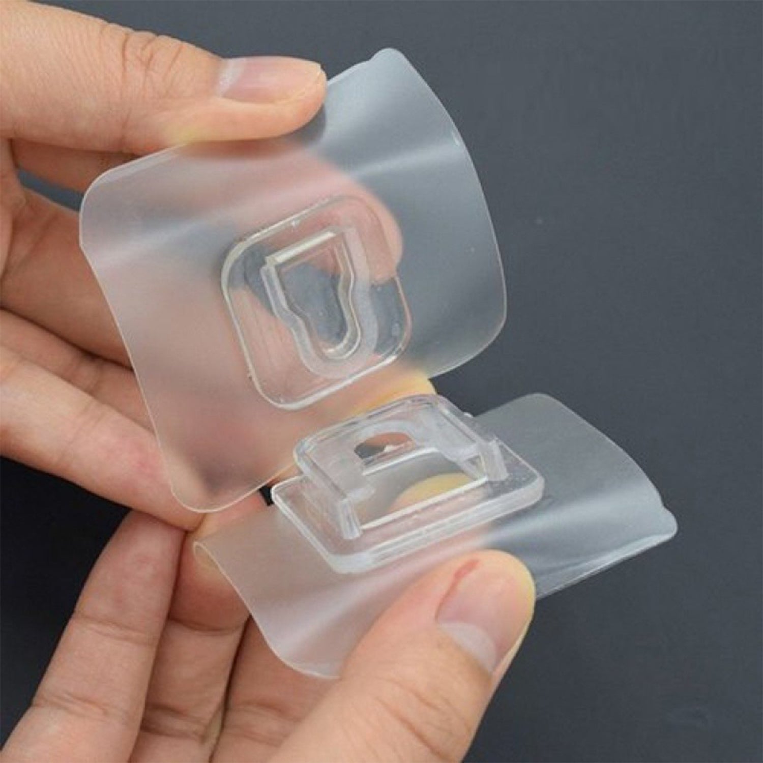 Two hands demonstrate how two clear adhesive hooks interlock to create a hanging mechanism.