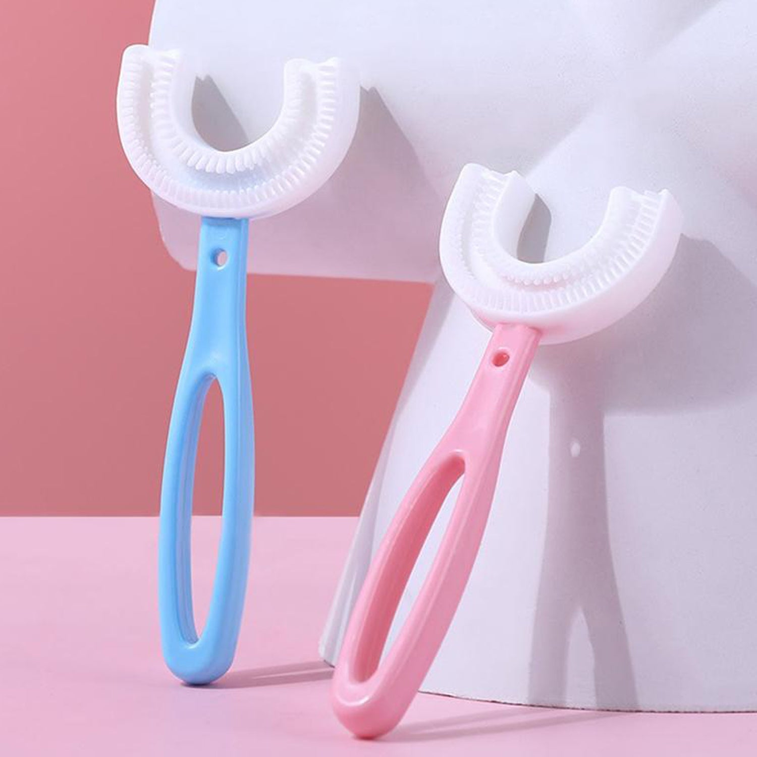 A light blue and a pink U-shaped toothbrush stand upright against a light pink and white background.