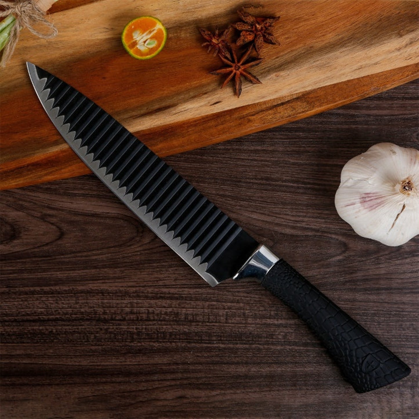 A black serrated chef's knife with a textured handle rests on a wooden board next to garlic and spices.