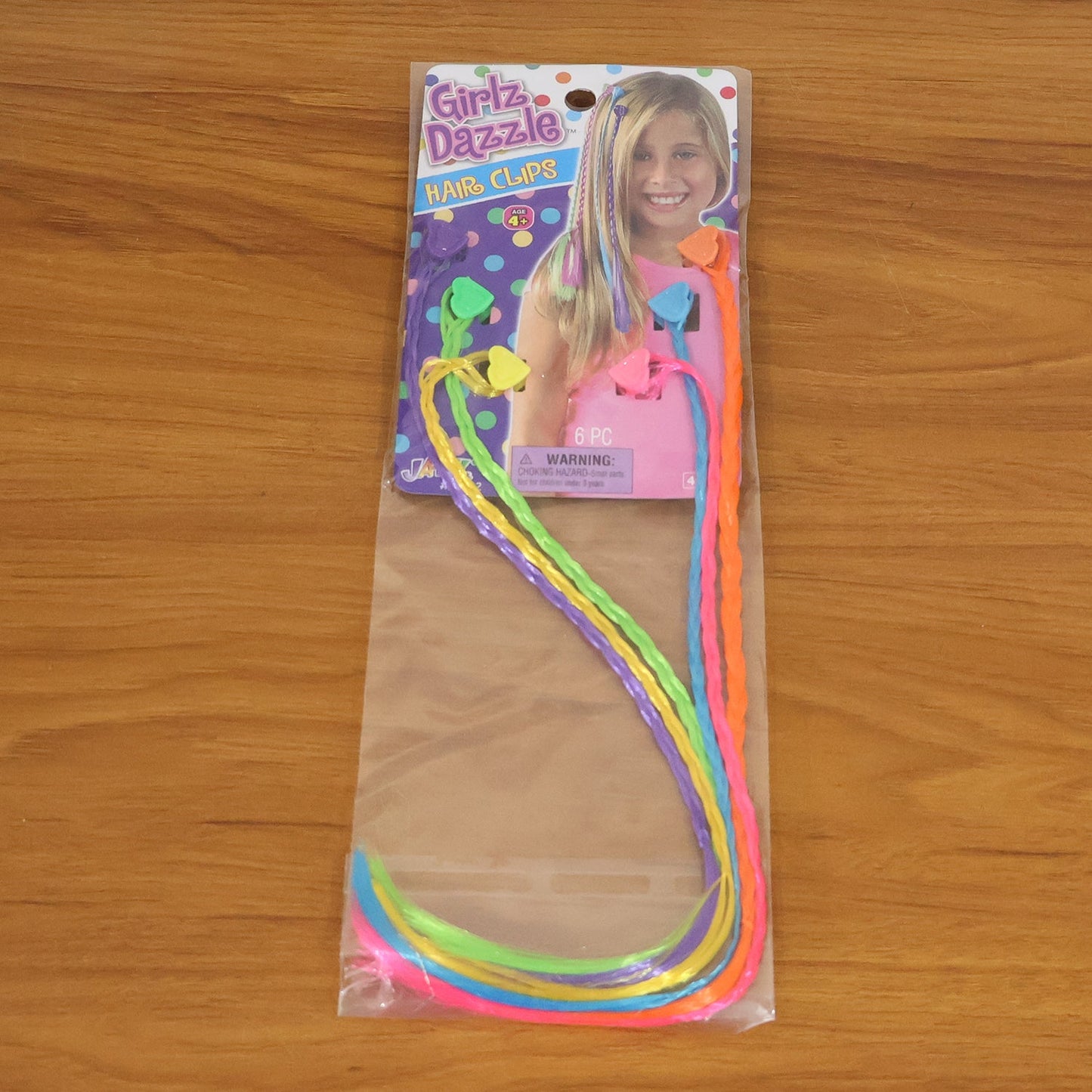 Six colorful braided hair extensions are sealed in clear plastic packaging with a colorful cardboard header.