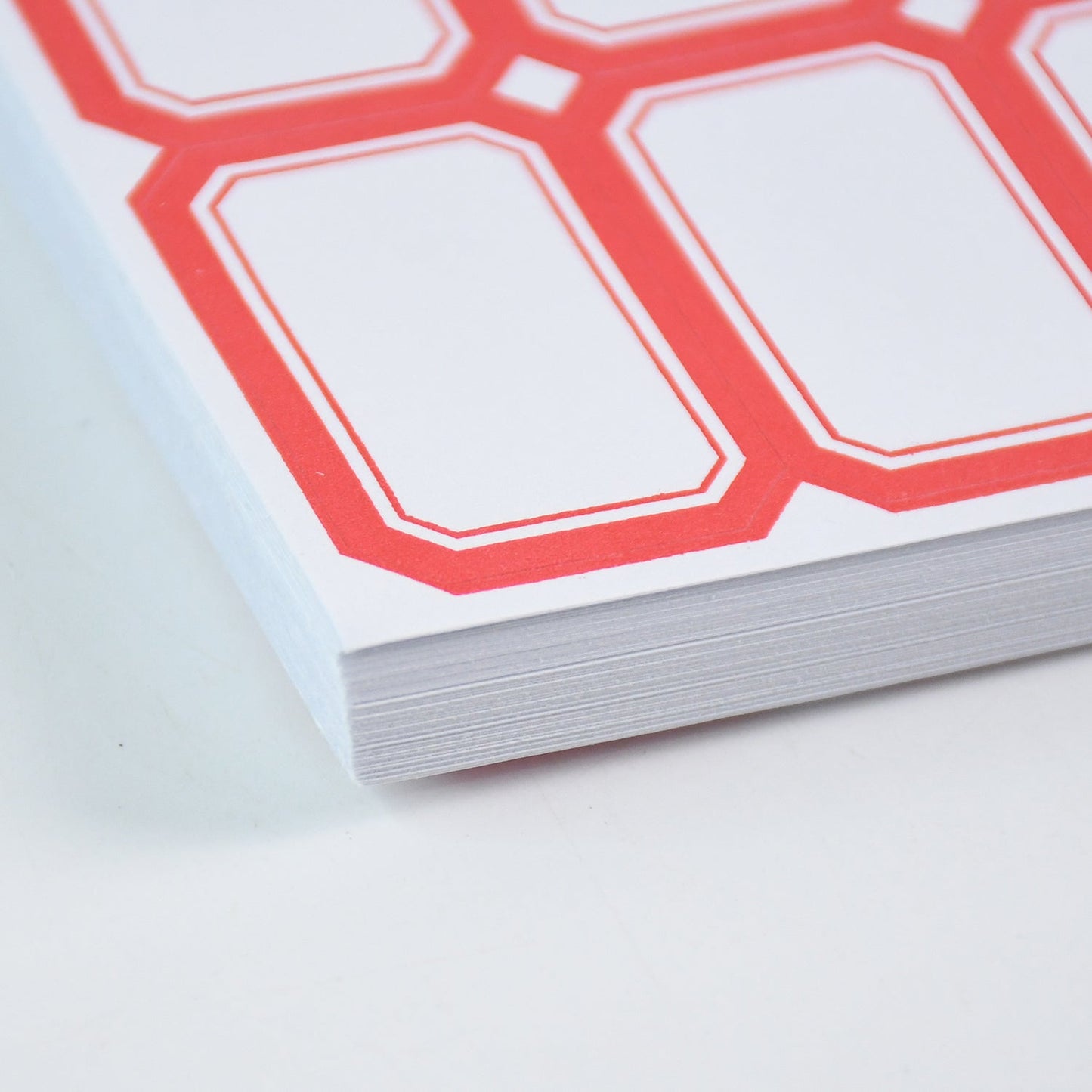 Close-up view of the corner of a stack of white labels with red borders.