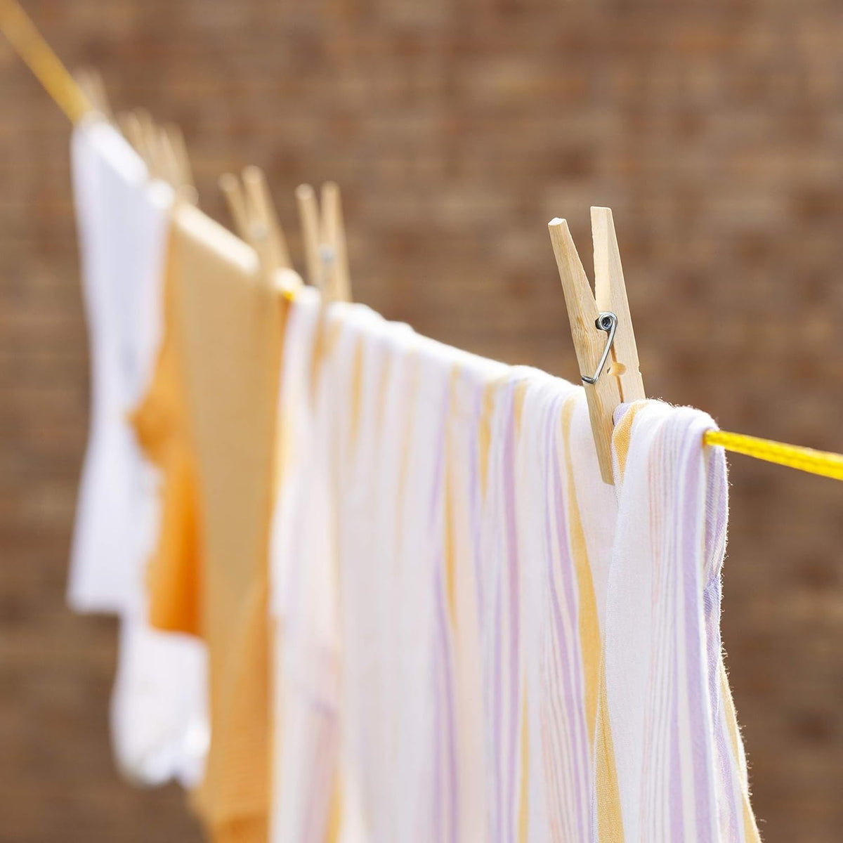 A bamboo clothes peg holding a striped white and purple shirt on a yellow clothesline with other clothes.