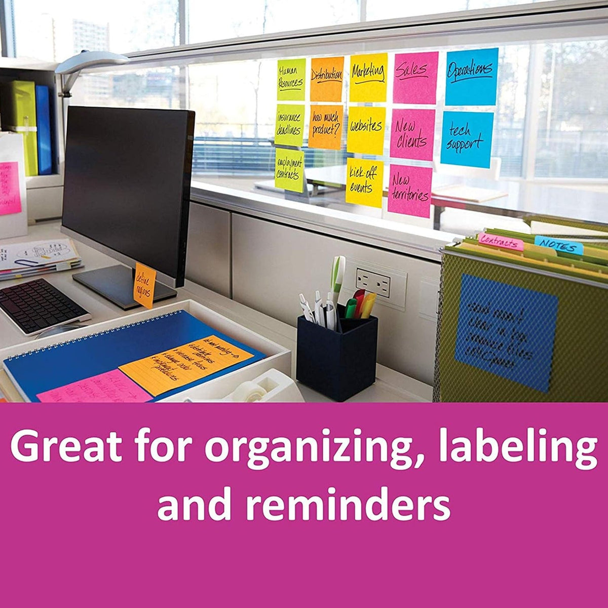 An office desk with a computer monitor, various office supplies, and colorful sticky notes attached to a clear partition and