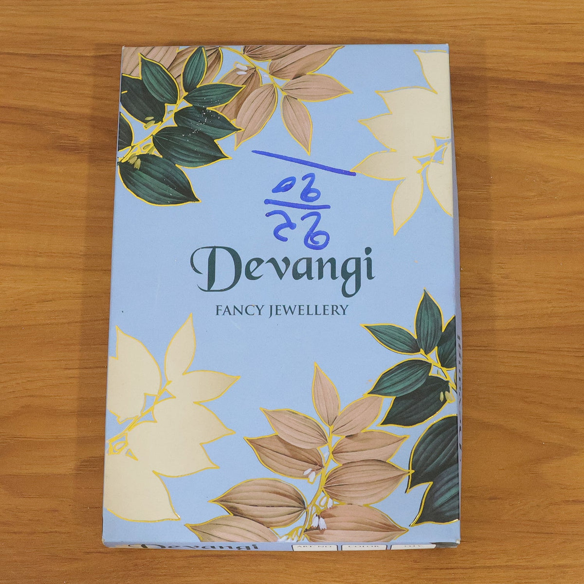 A light blue box with a floral design and the text "Devangi Fancy Jewellery" on a wooden surface.