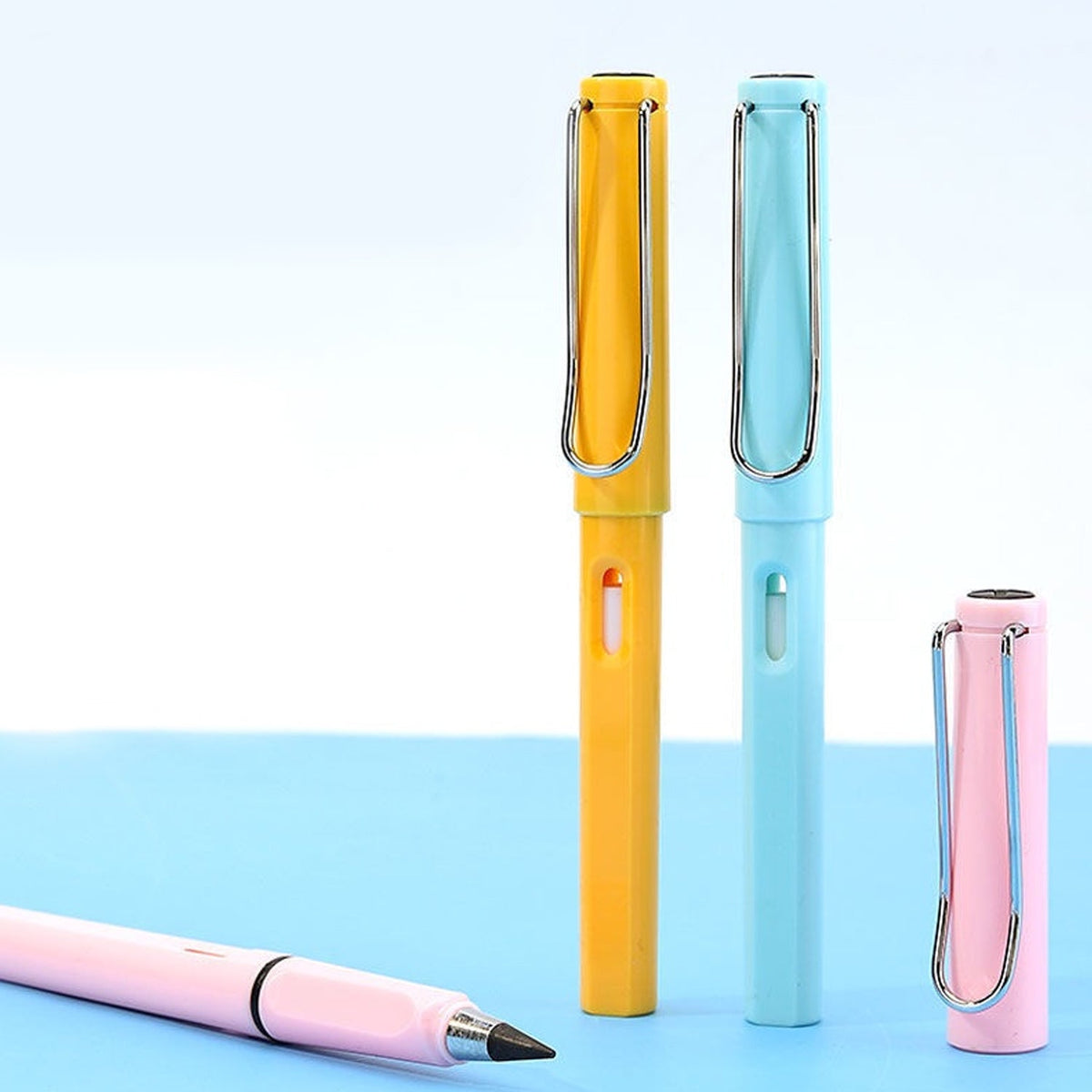 Three capped inkless pencils in yellow, blue, and pink stand upright on a blue surface.