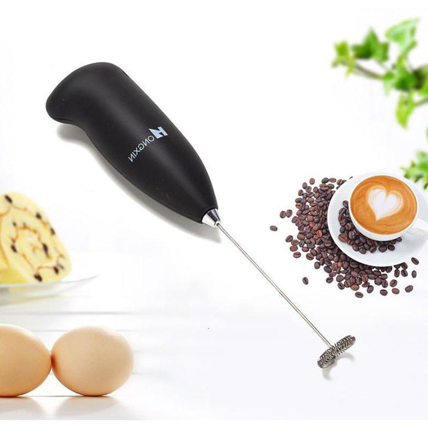 A black frother rests on a white surface next to coffee beans, a heart-shaped latte, and two eggs.