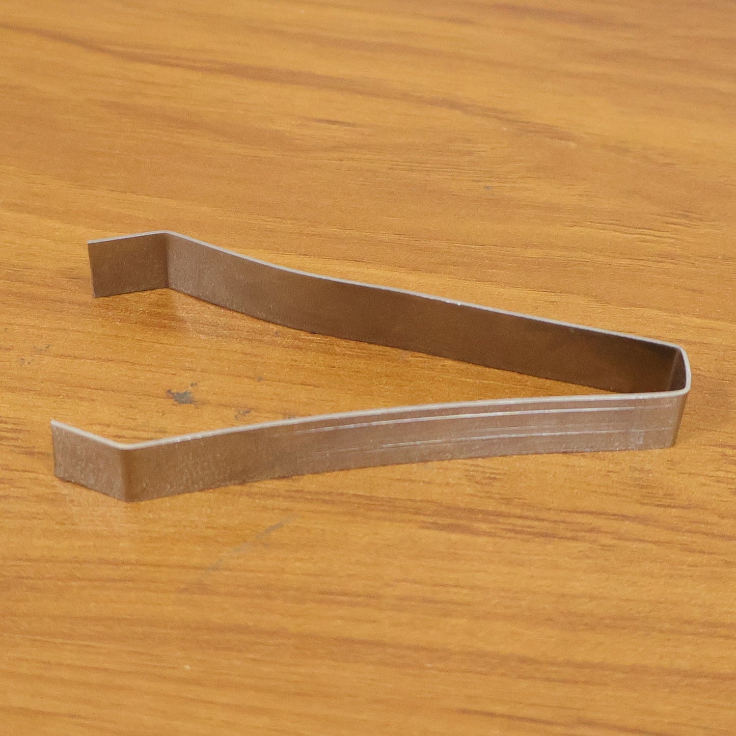 A single silver stainless steel tweezer rests on a light brown wooden surface.