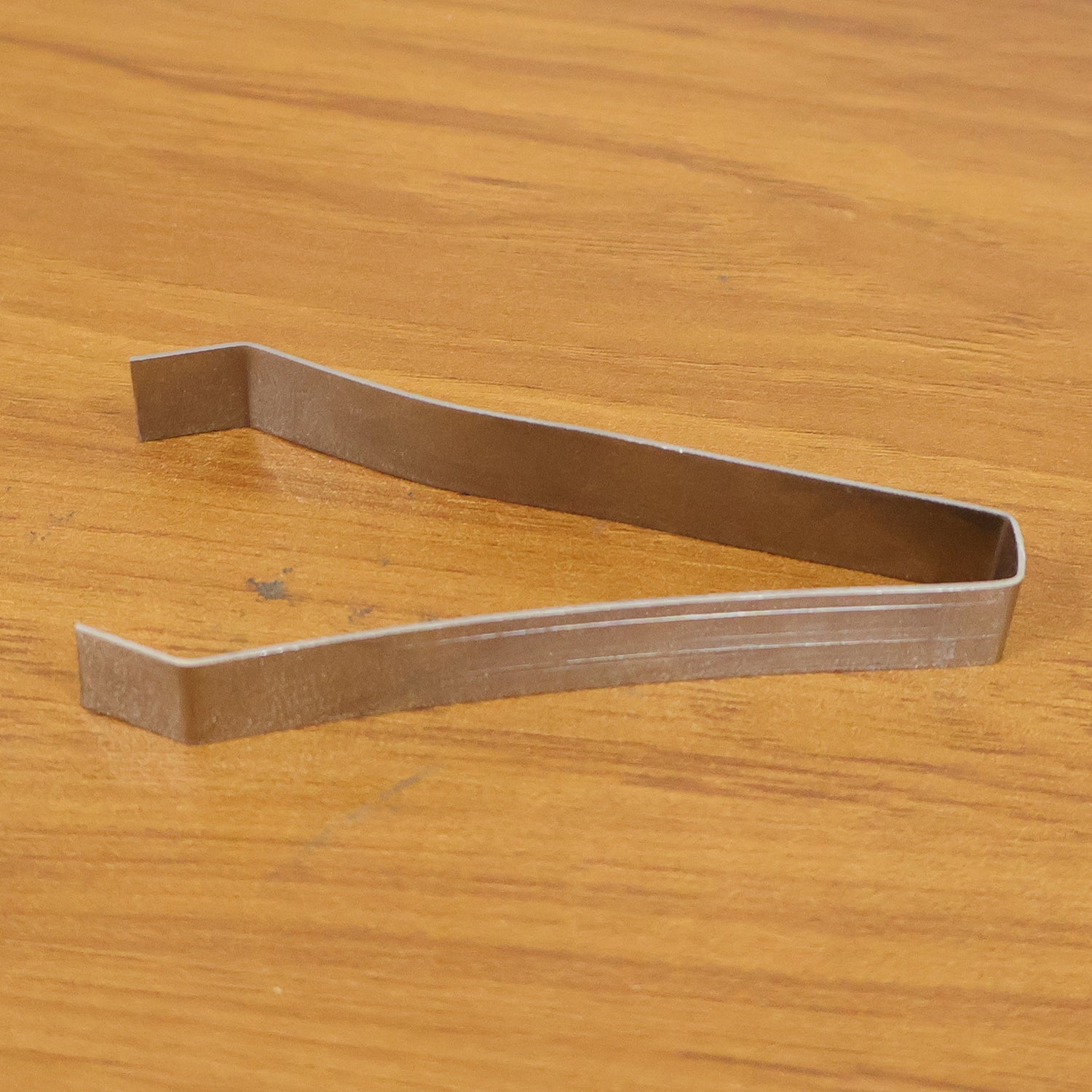 A single silver stainless steel tweezer rests on a light brown wooden surface.