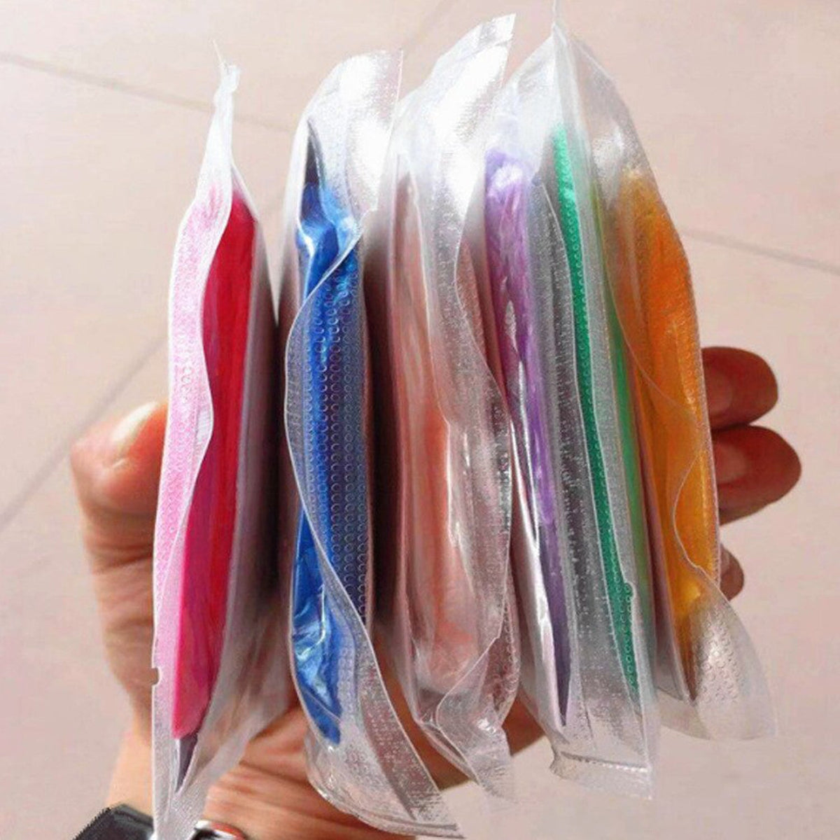 A hand holding several individually packaged, colorful compact rain ponchos in clear plastic sleeves.