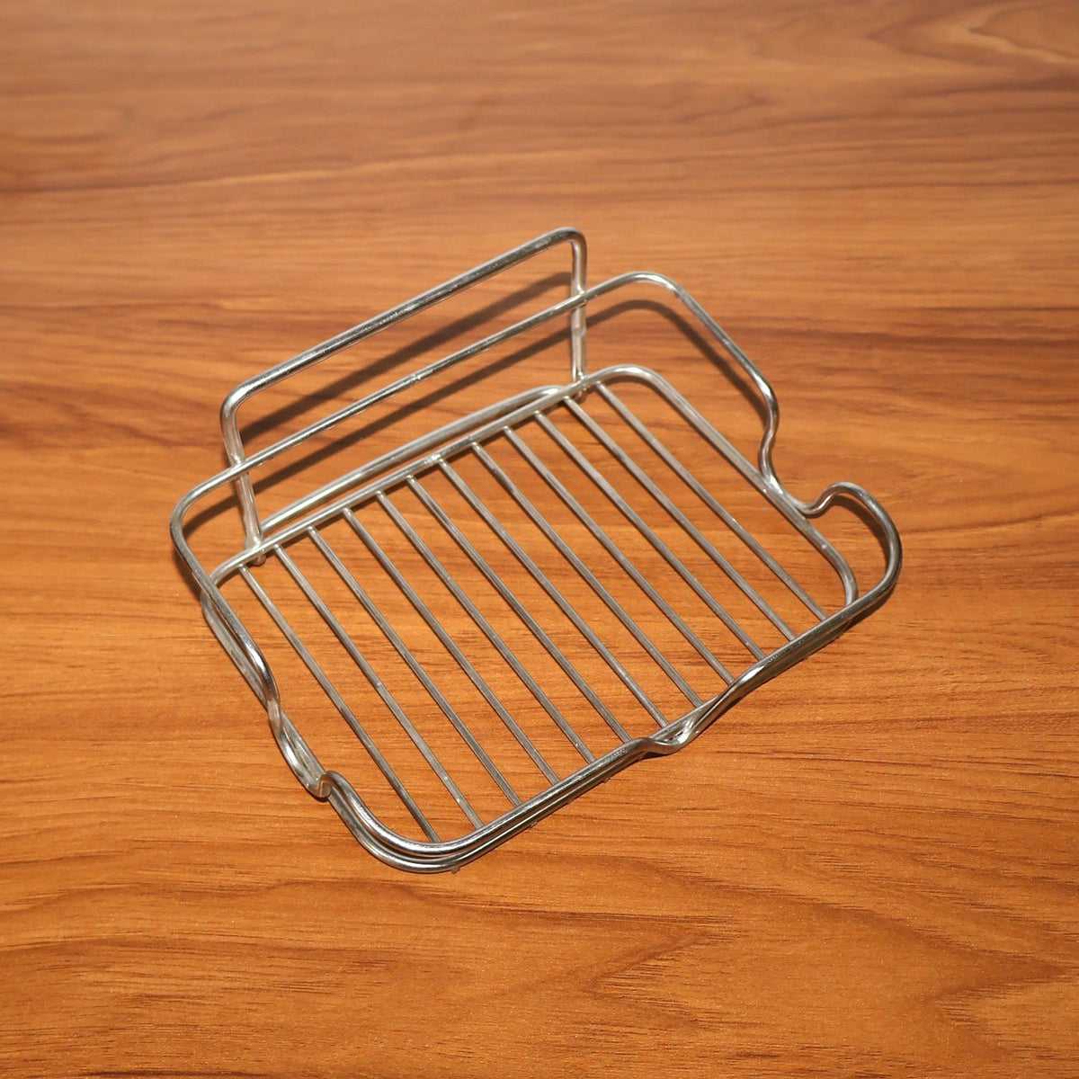 A stainless steel wire soap dish is angled on a dark wood surface, highlighting its wire construction.