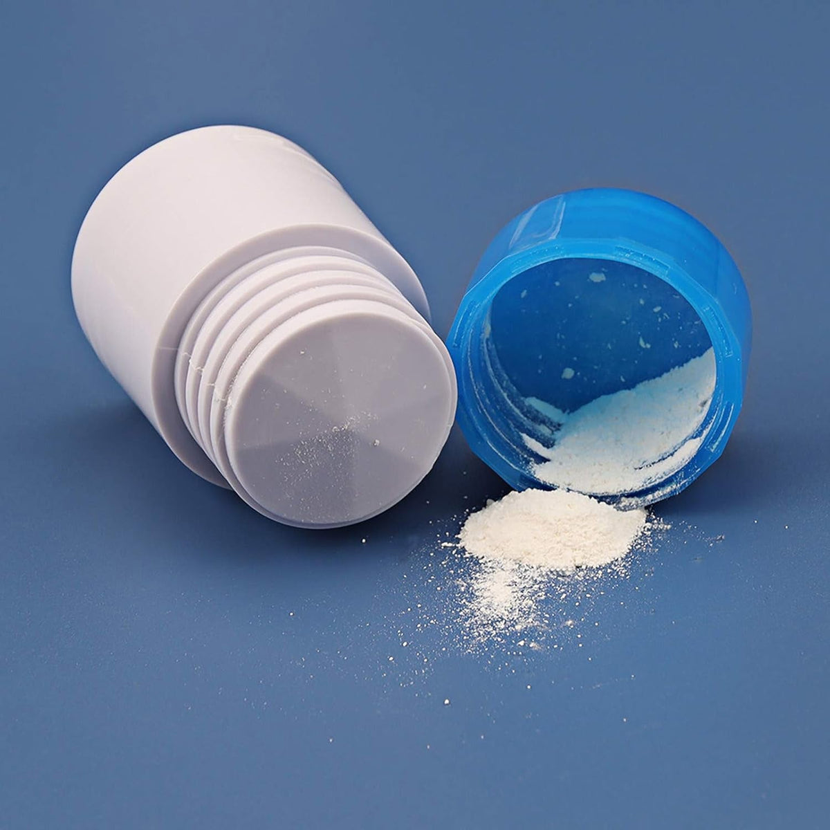 A white pill grinder component next to a blue cap with white powder spilled on a blue surface.