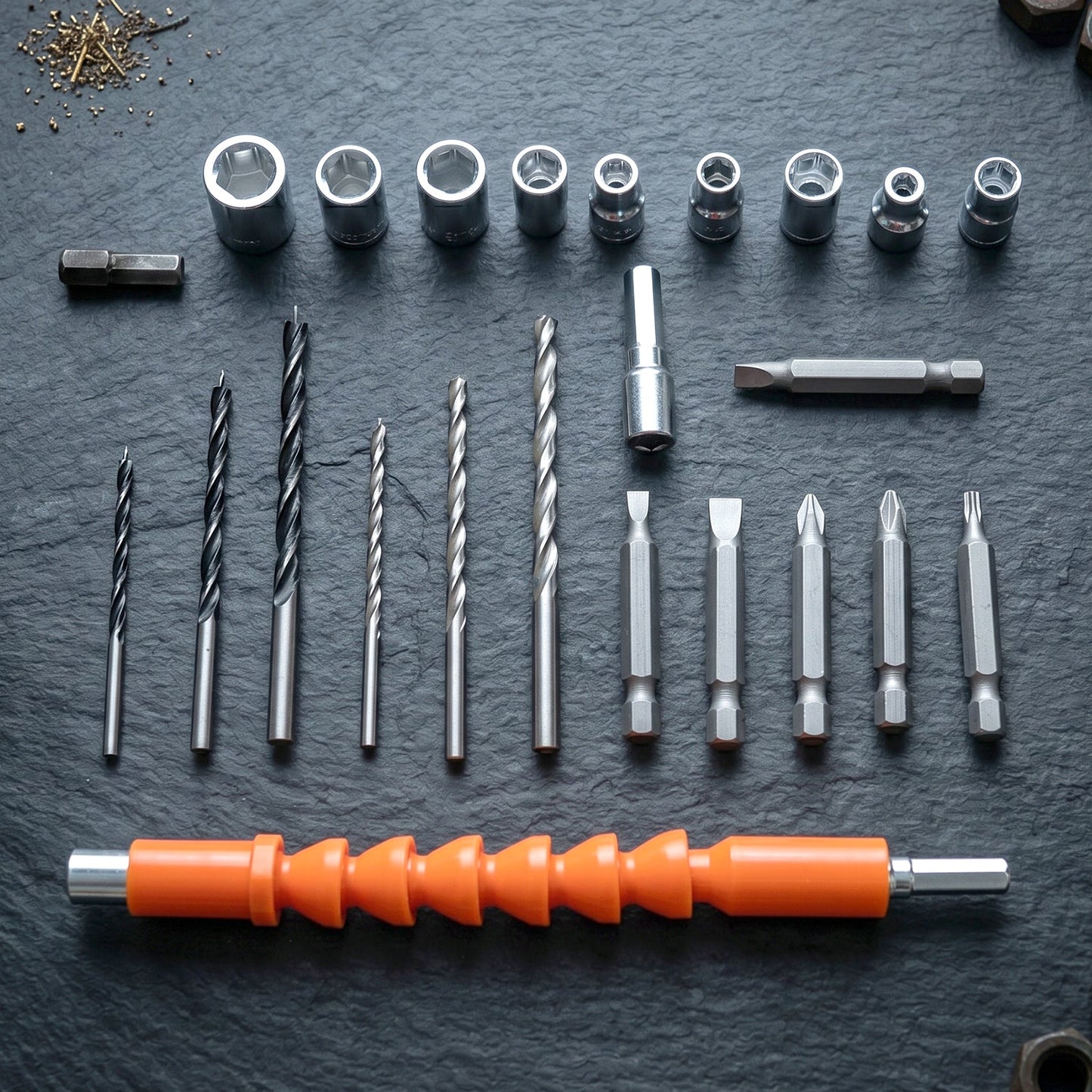 An array of drill bits, screwdriver bits, and socket wrenches neatly arranged on a dark, textured surface.