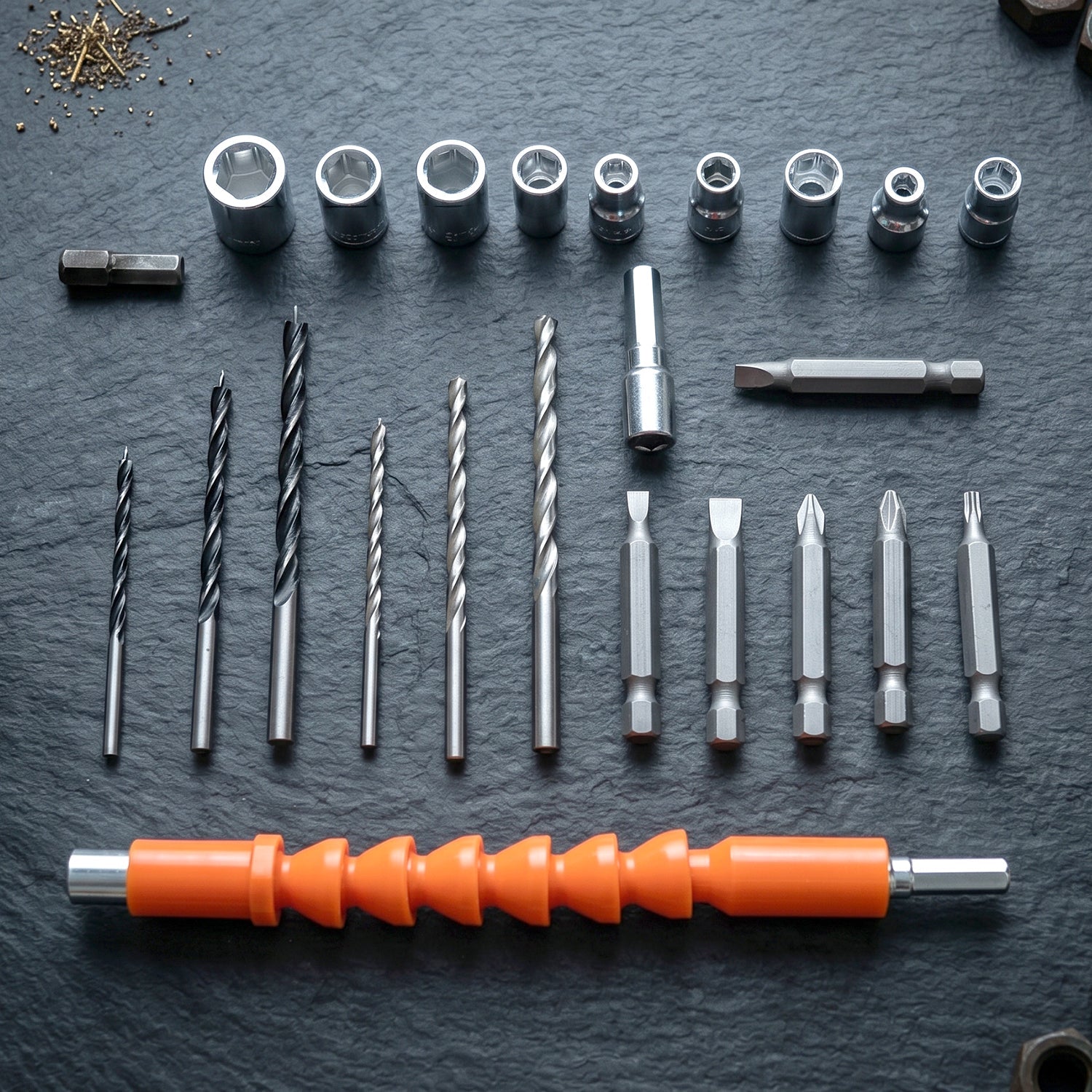 An array of drill bits, screwdriver bits, and socket wrenches neatly arranged on a dark, textured surface.