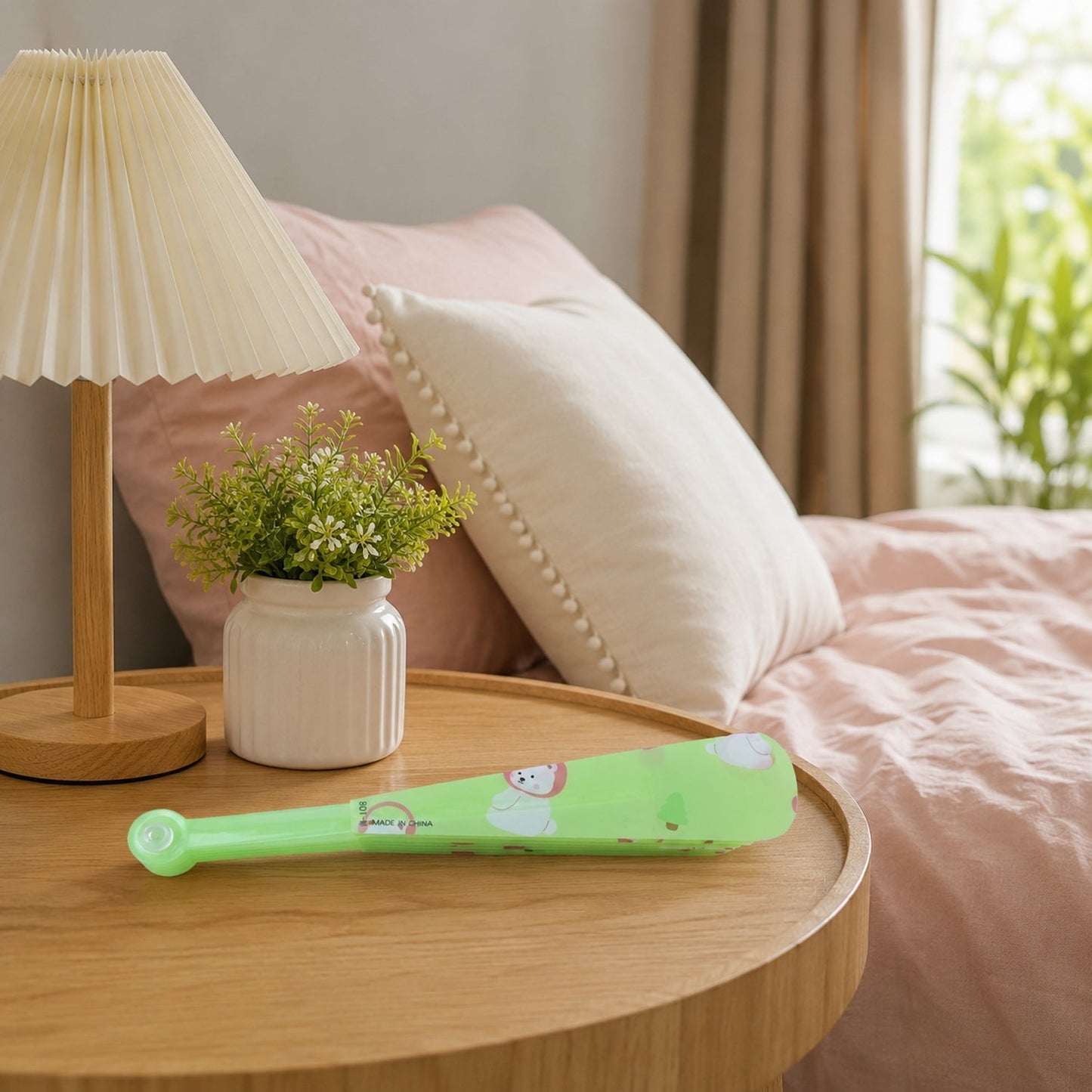 A folded green plastic fan with a bear and apple pattern rests on a wooden bedside table next to a lamp.