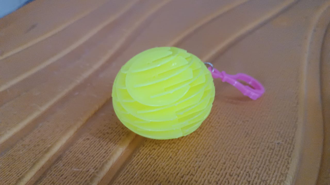 A bright green fully collapsed silicone ball keychain with a pink loop, resting on a textured brown surface.