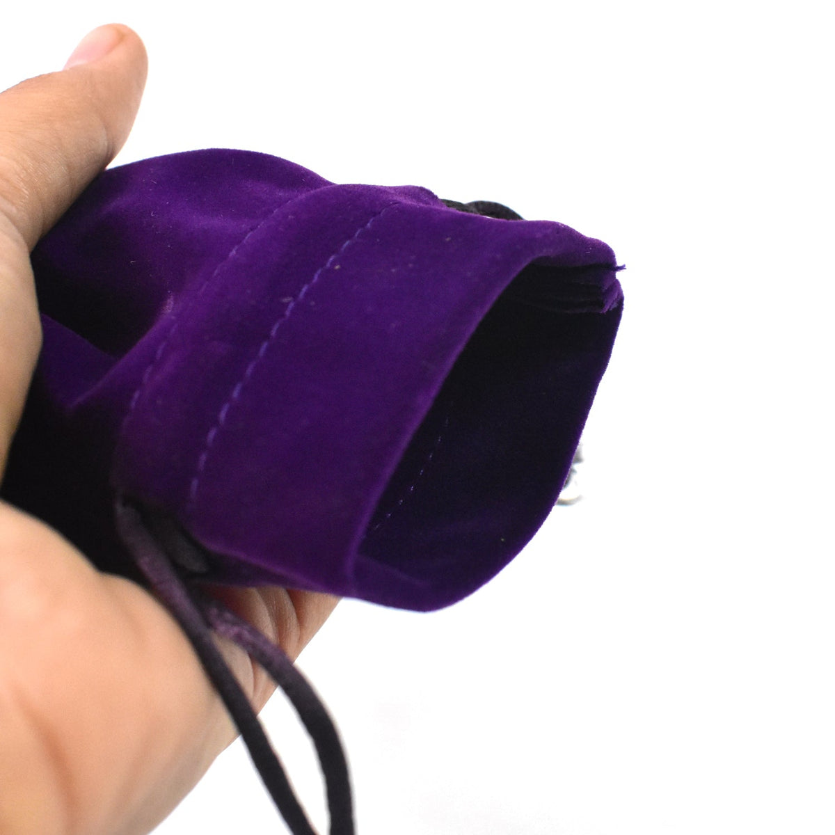 A hand holds open the top of a purple velvet drawstring bag, revealing its dark interior.