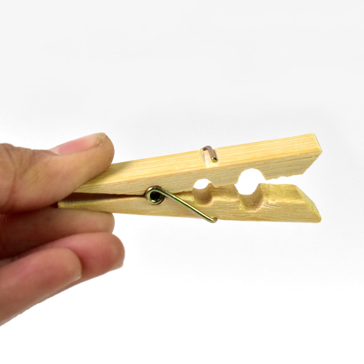 A hand holding an open bamboo clothes peg with a metal spring against a white background.