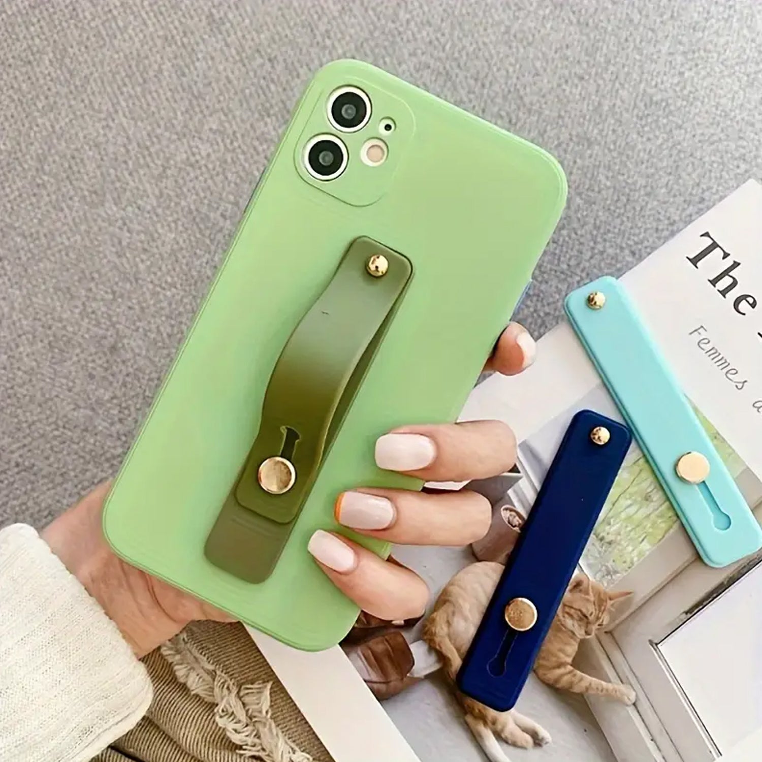 A hand holding a green phone with an olive green silicone grip attached, next to a dark blue and light blue grip.