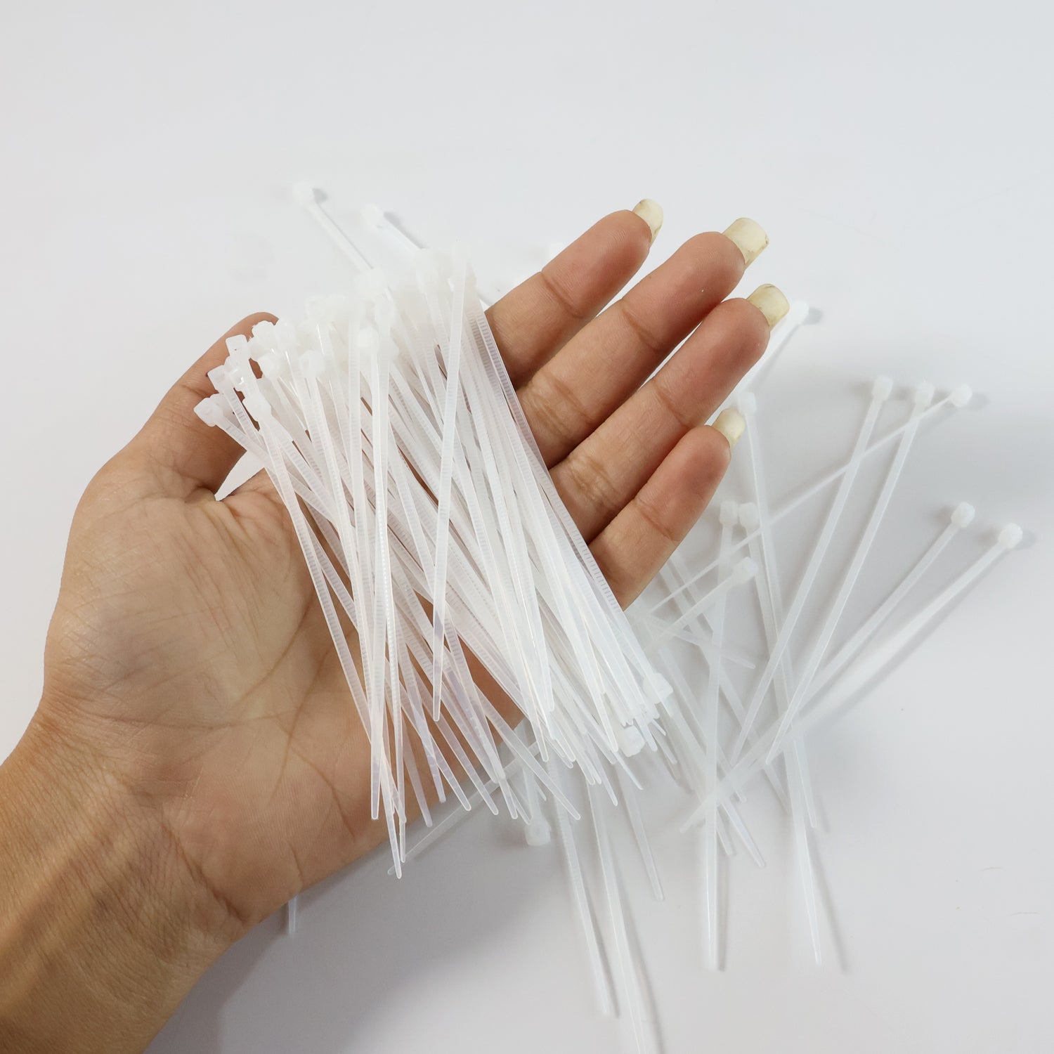 A hand holding a handful of white cable ties, with more ties scattered on a white surface.