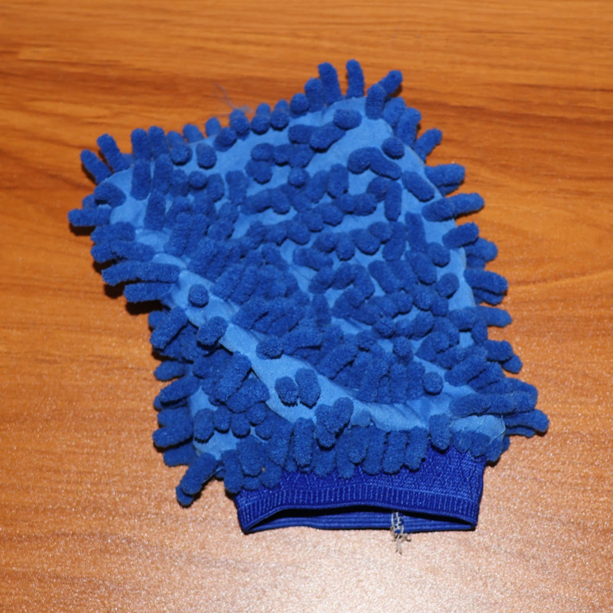 A blue microfiber wash mitt with an elastic cuff rests on a light brown wooden surface.